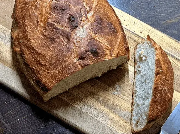 Freshly baked homemade bread with a golden, crispy crust on a wooden cutting board.