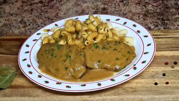A plate of pork medallions in a creamy mustard sauce with pasta, garnished with parsley.