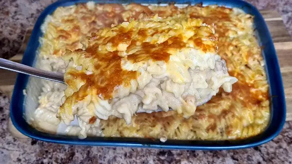A golden, bubbly serving of Tuna Mac & Cheese lifted from a baking dish, showing its creamy, cheesy layers.