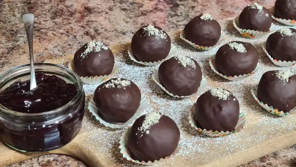 Chocolate-covered walnut balls with a sprinkle of crushed walnuts, neatly arranged on a wooden board.