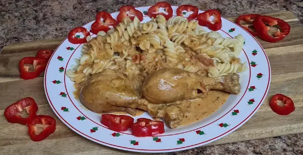 A plate of Hungarian chicken paprikash with creamy sauce, served with pasta and garnished with fresh red pepper slices.