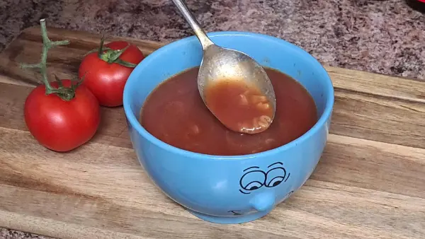 A comforting bowl of tomato soup with alphabet pasta, sitting on a wooden board next to fresh tomatoes.