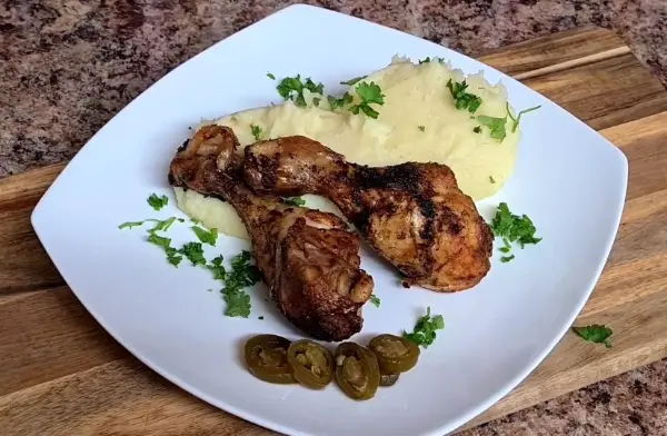Crispy chicken drumsticks served with creamy mashed potatoes, topped with parsley and jalapeño slices on a white plate.