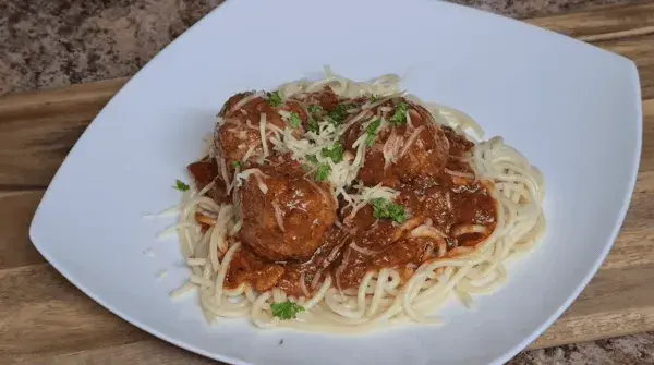 A hearty plate of spaghetti topped with meatballs in rich tomato sauce, garnished with cheese and parsley, served on a rustic wooden board.
