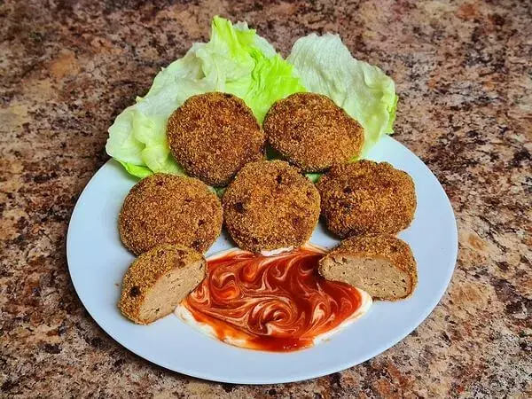 Golden and crispy meatballs served on a white plate with fresh lettuce and a swirl of ketchup for dipping.