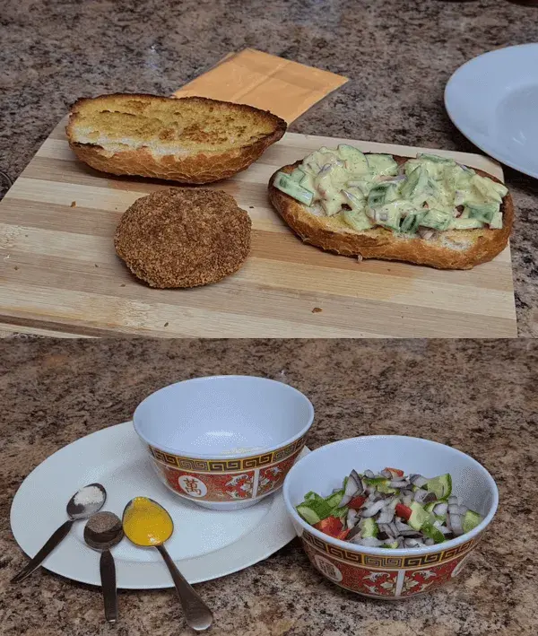 Preparation of crispy gold stack sandwich: crispy fried patty, fresh cucumber salad topping, sliced cheese, toasted buns, and various sauces arranged on a wooden cutting board and countertop.