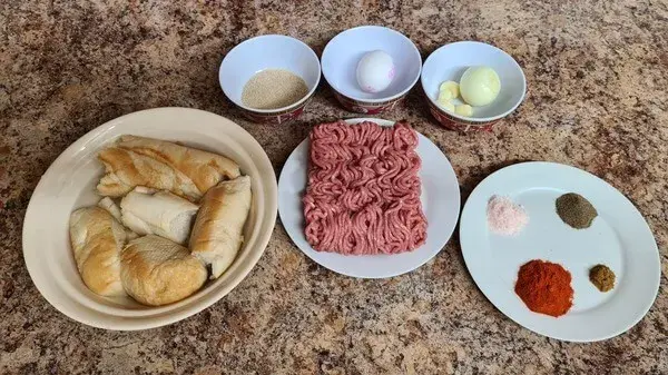 Ingredients for golden and crispy meatballs: ground meat, bread rolls, breadcrumbs, eggs, onions, garlic, and various spices arranged neatly on a countertop.