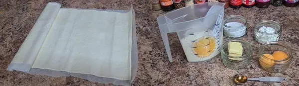 Ingredients for puff pastry dessert: puff pastry sheets, milk, eggs, butter, sugar, flour, and vanilla extract arranged neatly on a countertop.