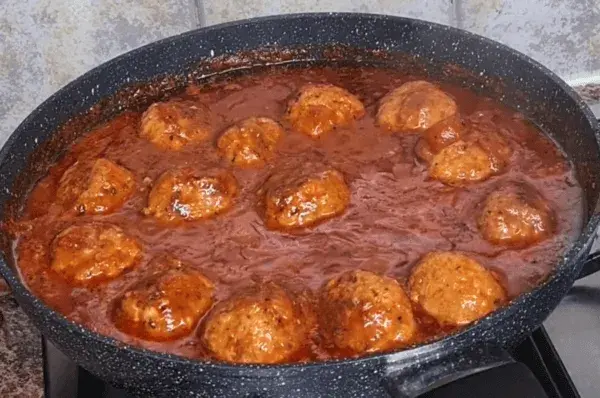 Homemade meatballs simmering in rich tomato sauce in a large pan on the stove.