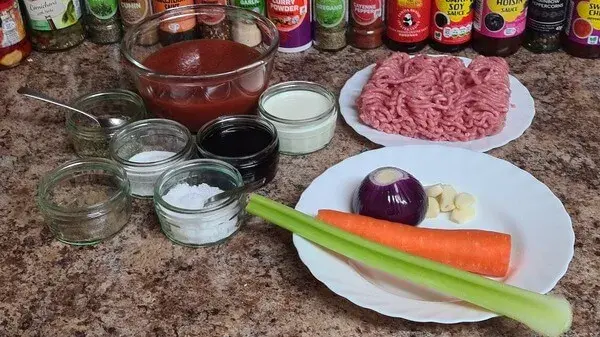 Ingredients for homemade lasagna: ground meat, tomato sauce, cream, Worcestershire sauce, flour, spices, red onion, garlic cloves, carrot, and celery neatly arranged on a kitchen counter.