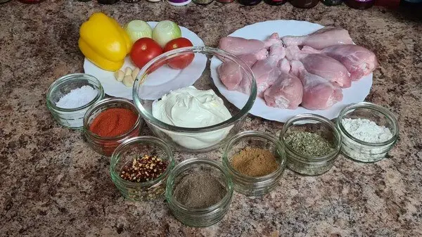Ingredients for easy sour cream chicken paprikash: chicken drumsticks, sour cream, onions, tomatoes, bell pepper, garlic, paprika, chili flakes, spices, and herbs arranged neatly on a countertop.
