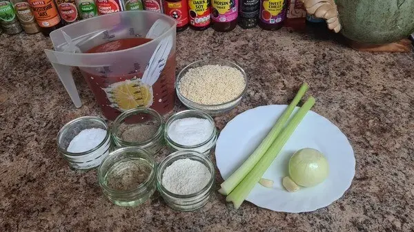Ingredients for homemade tomato soup: tomato passata, alphabet pasta, celery stalks, onion, garlic cloves, flour, vegetable oil, salt, sugar, and spices arranged neatly on a countertop.
