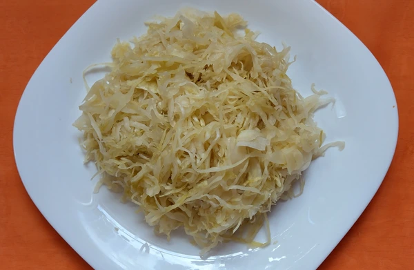 Plate of traditional sauerkraut on a white dish, placed on an orange tablecloth.