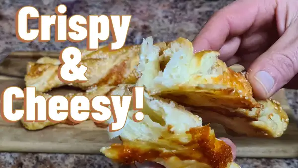Hand holding a warm, flaky cheese twist with melted cheese inside and golden crust