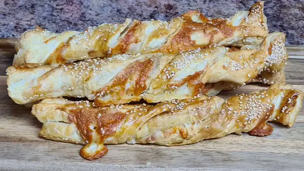 Golden-brown cheese twists on a wooden board with sesame seeds on top