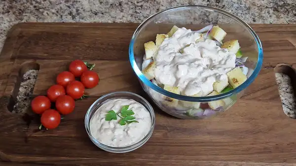 Homemade Thousand Island dressing poured over a colorful salad with croutons, red onion, cucumber, and cherry tomatoes, next to a small bowl of extra sauce.