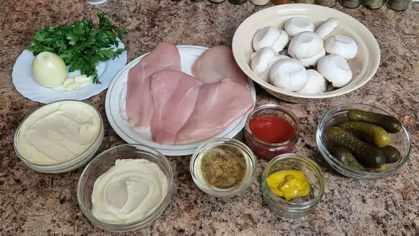 Ingredients for Chicken Stroganoff laid out on a countertop: raw chicken breasts, fresh mushrooms, sour cream, double cream, mustard, tomato passata, pickles, parsley, onion, garlic, and seasonings in small glass bowls.