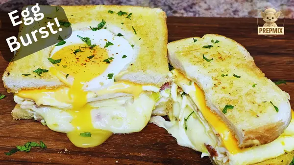 Crispy breakfast sandwich with a runny egg yolk melting through toasted bread, layered with ham and double melted cheese on a wooden board.