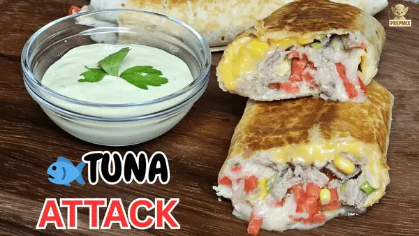 Golden toasted cheesy tuna wrap cut open with creamy tuna filling, melted cheese and fresh vegetables, served with dipping sauce