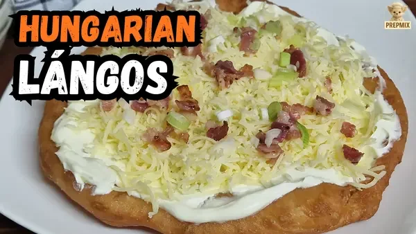Traditional Hungarian lángos topped with garlic, sour cream, grated cheese, crispy bacon and spring onions, served on a white plate.