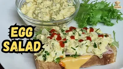 Loaded egg salad toast with creamy chunky egg salad, ham, cheese, curly lettuce, Sriracha and fresh chives.