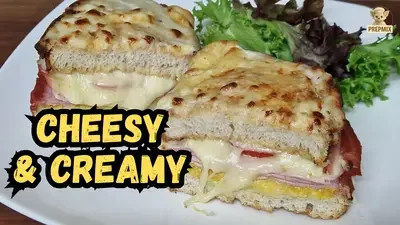 Two crispy ham and cheese sandwiches filled with ham, tomato, mozzarella and creamy cheese sauce, topped with melted golden cheese and served with fresh salad.