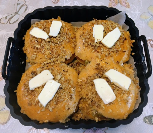 Golden baked rhubarb crumble buns topped with chopped walnuts and melting butter pieces in a black baking tray.